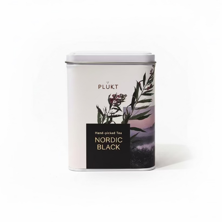 A white metal tea tin with a silver lid and a label featuring green botanical leaves, purple flowers, and a black block with gold text reading &
